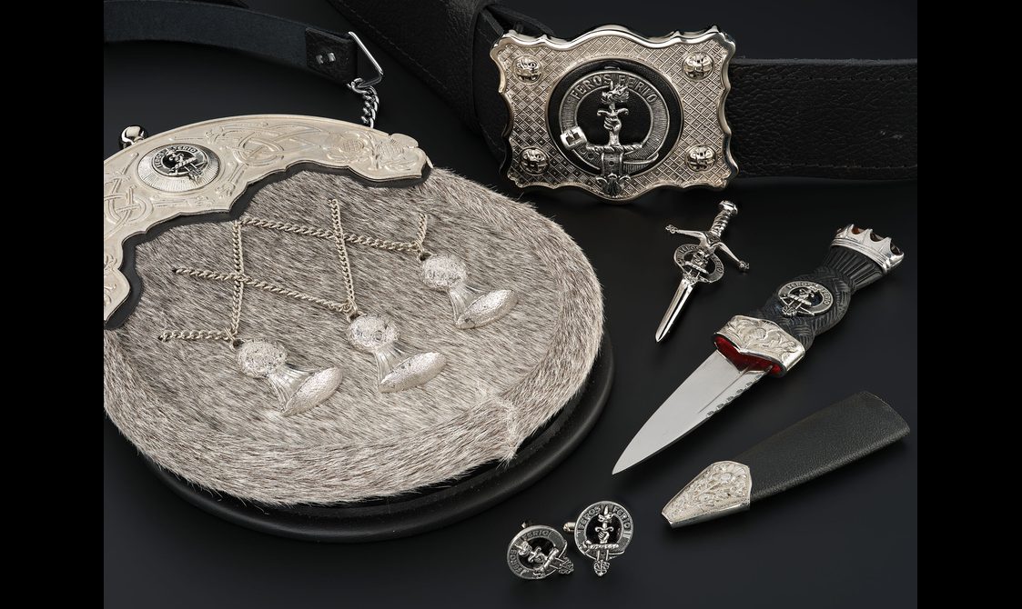 Various accessories for a kilt outfit including a sporan with a textured surface and thistle decoration, a belt, cufflinks, a pin, and a dagger and sheath.