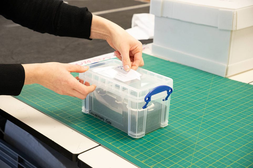 A curator placing a labelled card into a plastic sleeve on a storage box.
