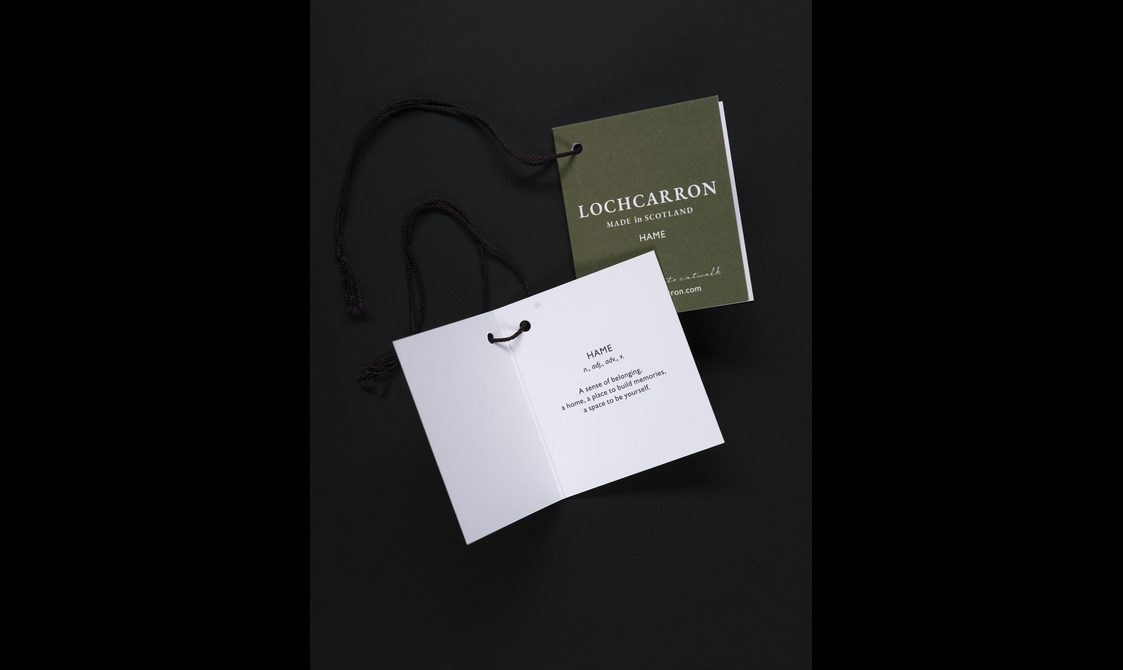 Two clothing tags, one has a green front, the other is open with text. Both are threaded with black string.