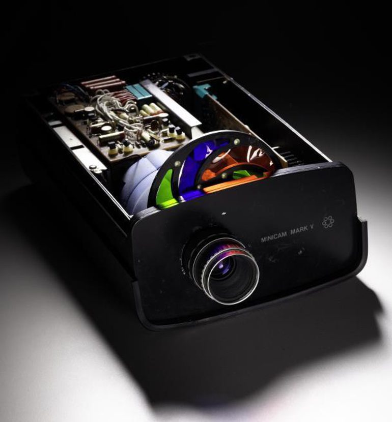 A flat rectangular video camera with its top open to reveal a colourful disk and inner workings