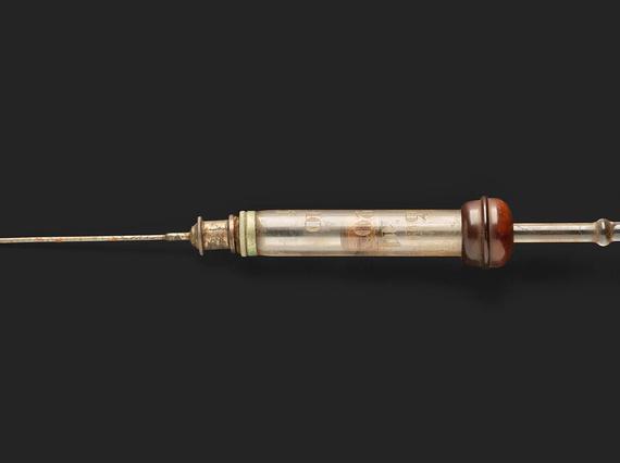 A vintage glass syringe with a needle attached.