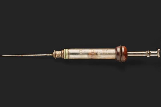 A vintage glass syringe with a needle attached.
