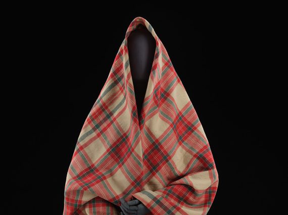 A mannequin wearing a red and cream tartan shawl.