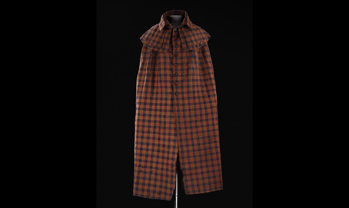 A mannequin wearing a long brown, navy, and red tartan cloak