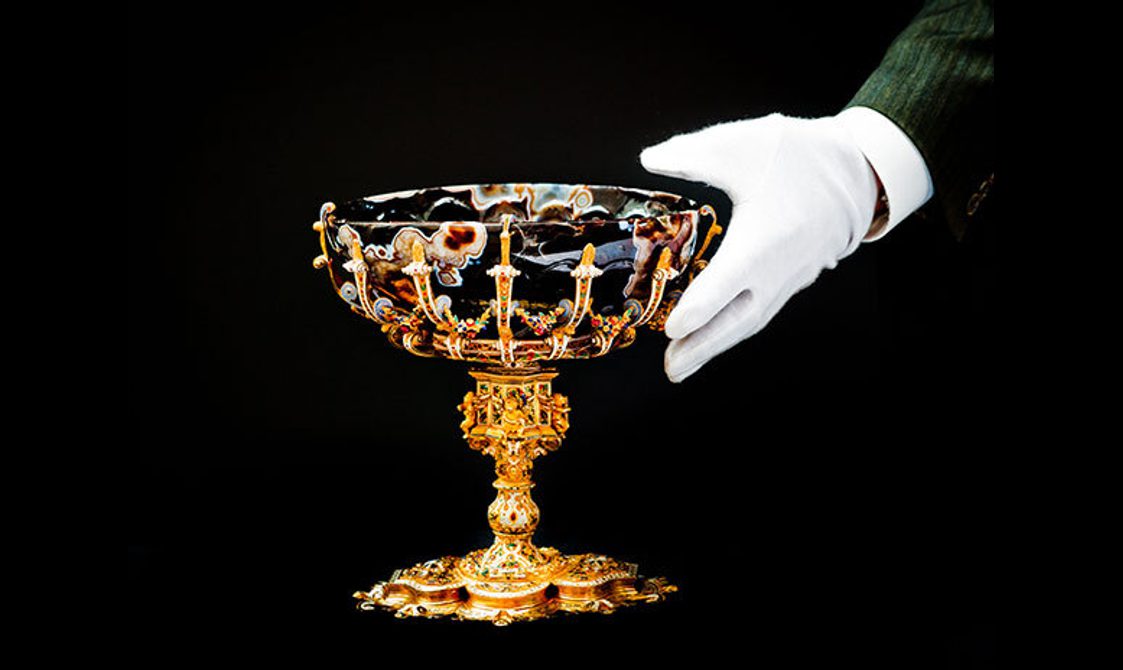 A curator's hand positioning a sardonyx bowl with an enamelled gold foot.