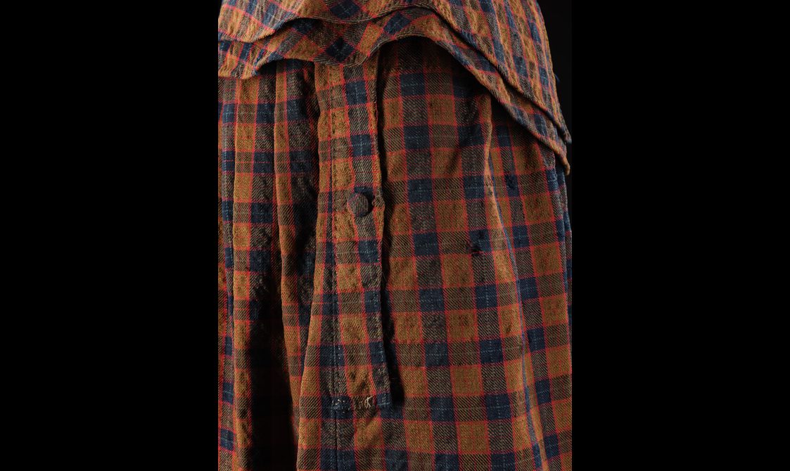 A detail of a brown, navy, and red tartan cloak with buttons down the front