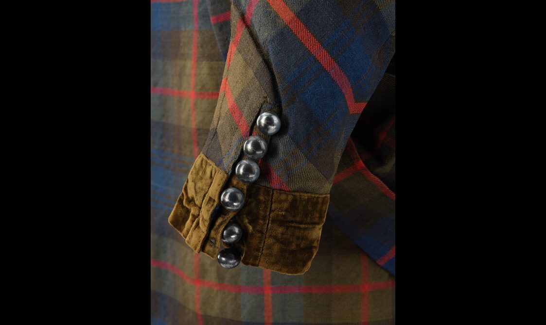 Detail of a navy, red, and green tartan jacket with a velvet and buttoned cuff.