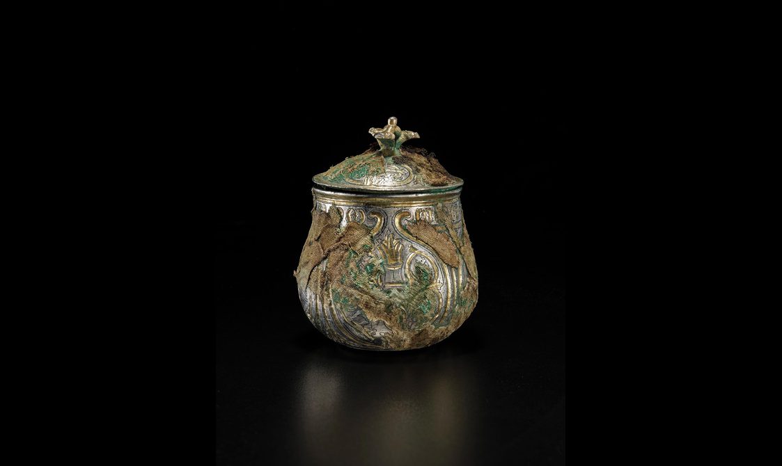 A silver round vessel with a gilded lid engraved with various round and organic shapes
