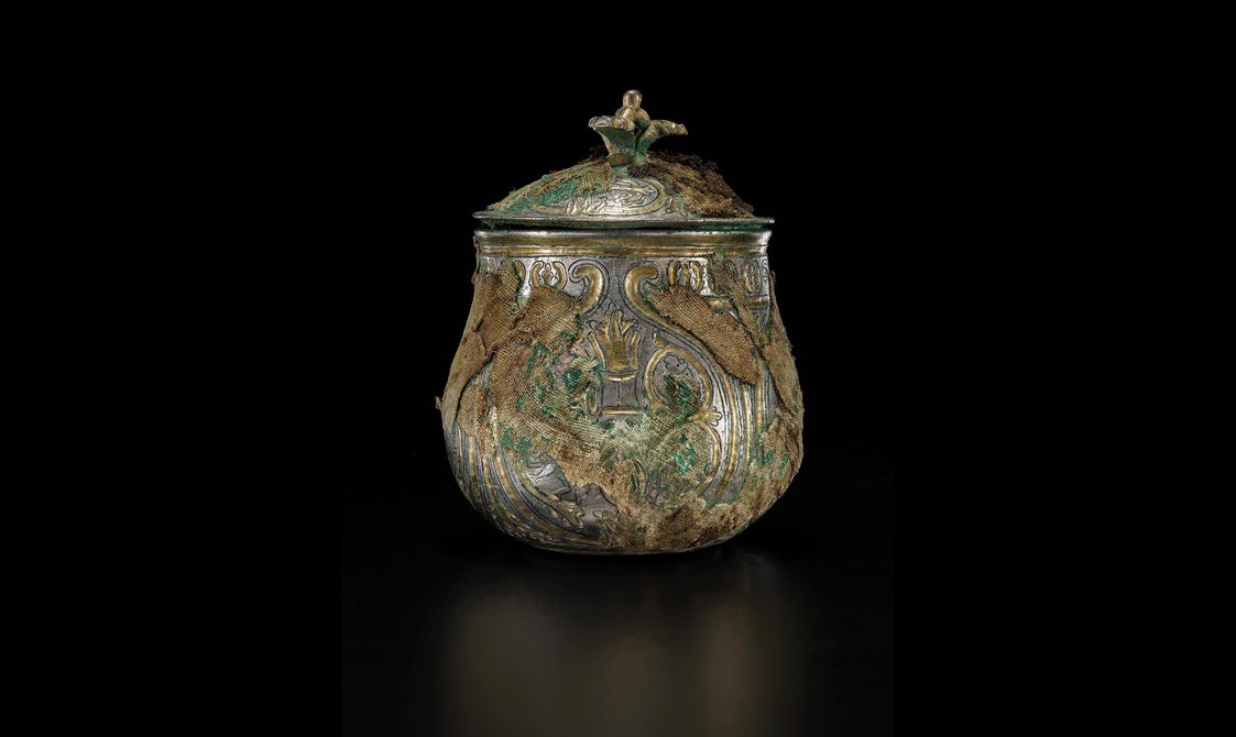A silver round vessel with a gilded lid engraved with various round and organic shapes
