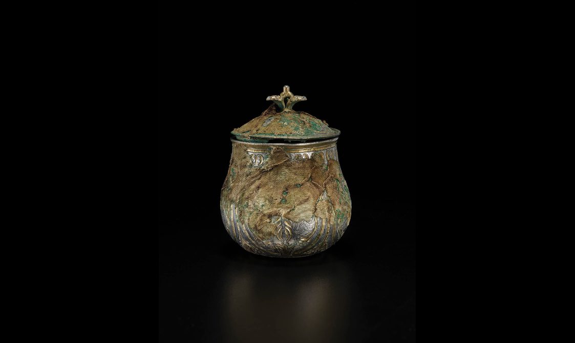 A silver round vessel with a gilded lid engraved with various round and organic shapes.