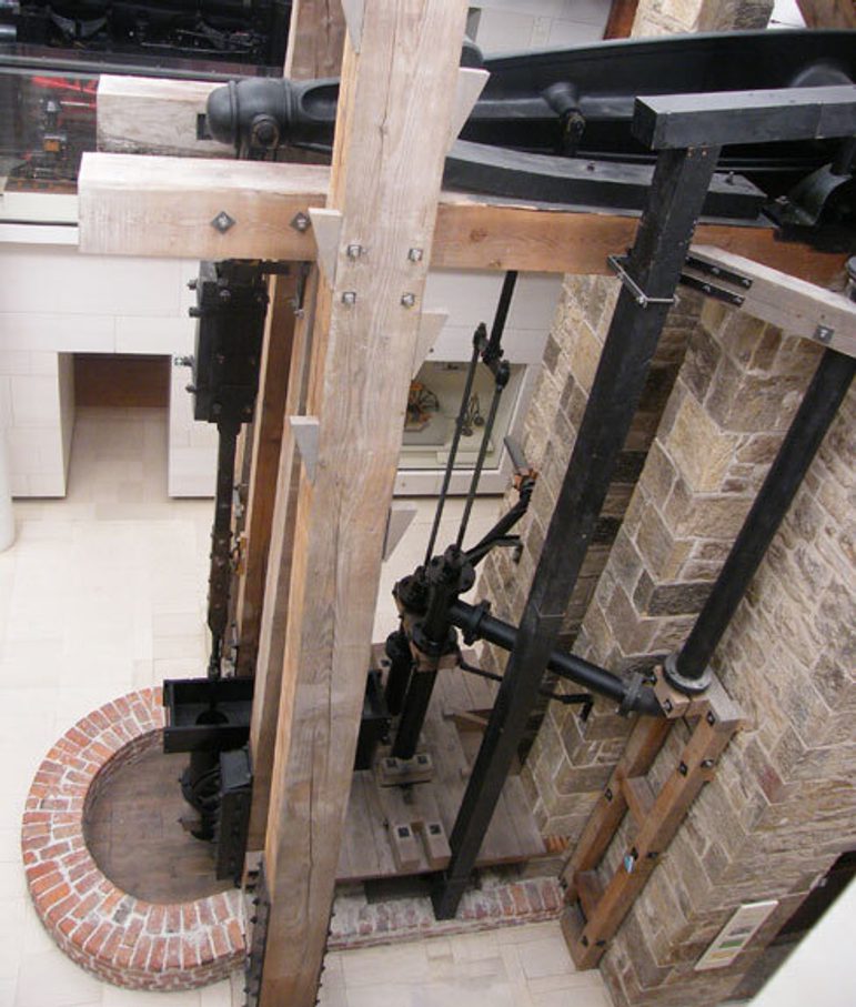 A large engine made of steel supported by wooden beams attached to a brick building.