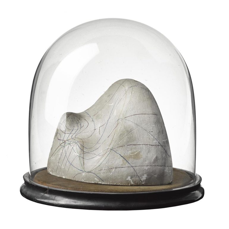 A white plaster cast object with coloured lines on its surface sitting on a wooden disc covered with a glass dome top.