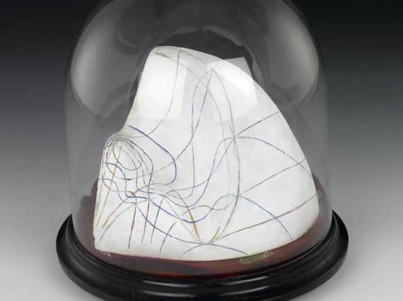 A white plaster cast with coloured lines drawn all over its surface, sitting on a wooden disc covered with a glass dome.