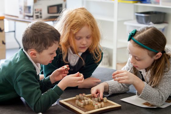 Three primary school pupils are gathered around and are playing a board game.