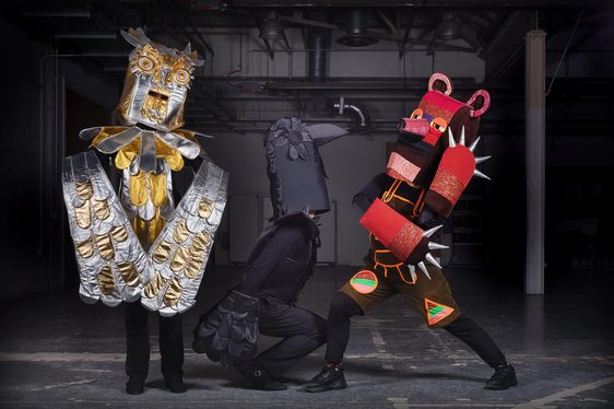 Three performers dressed in colourful outfits. On the left is a gold and silver owl, a black raven is in the middle, and a red bear is on the right.