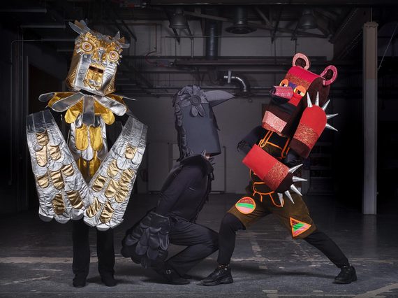 Three performers dressed in colourful outfits. On the left is a gold and silver owl, a black raven is in the middle, and a red bear is on the right.