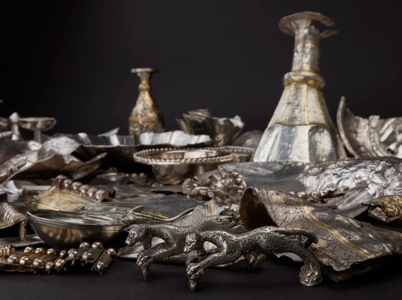 Mass of hacked silver objects including plates, cups, and two speckled figurines of panthers or lionesses.