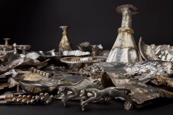 Mass of hacked silver objects including plates, cups, and two speckled figurines of panthers or lionesses.