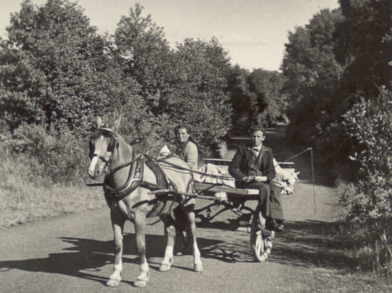 A black and white photograph of a man and woman sitting in a horse drawn cart on a country road.