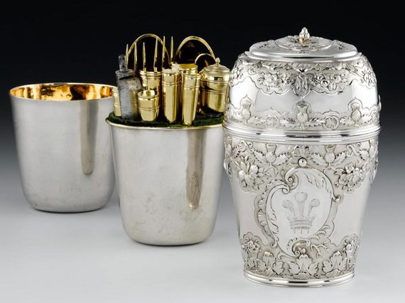 Three silver cylinder shaped boxes, placed behind each other, first box with the lid is decorated in leaf and scottish thistle motifs and a crown with three feathers in the center. Two boxes are plain silver with gilded interior. The middle box contains gold cutlery.