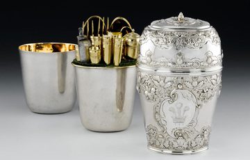 Three silver cylinder shaped boxes, placed behind each other, first box with the lid is decorated in leaf and scottish thistle motifs and a crown with three feathers in the center. Two boxes are plain silver with gilded interior. The middle box contains gold cutlery.