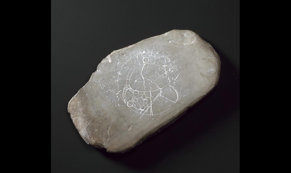 A light grey stnoe with an etching on its surface of a round object with some Celtic details