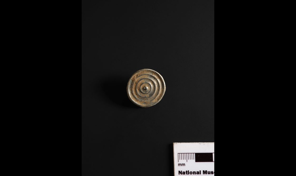 A circular bronze button. There are four concentric circles within the button's design.