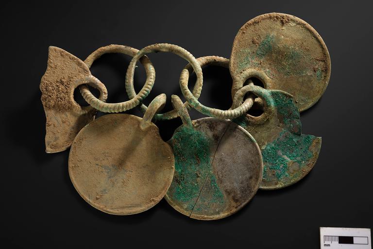 Three bronze rings linked together in a row. Five bronze disks are hanging from these rings, creating a rattle.