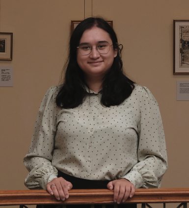 A woman dressed in a white polka dot blouse holding on a balustrade.