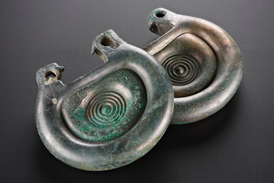 A bronze fitting that is silvery in colour with some green corrosion on the surface. It's rounded, with a concentric circle design.