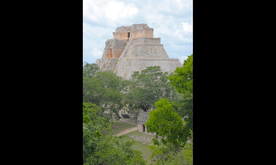 View of the Mayan ruins at Uxmal, surrounded by lush greenery under a cloudy sky.