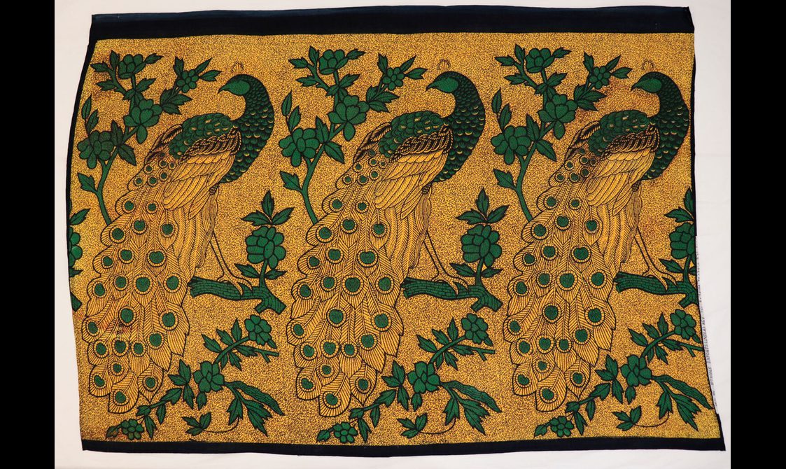 Gold textile with pattern of large black and green peacocks perched on branches.