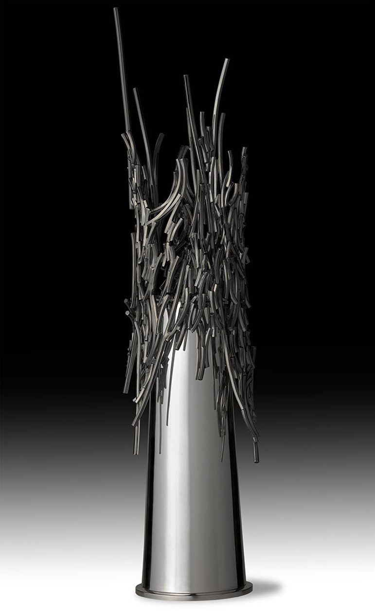A tall silver vase with a plain silver stem with jagged bits of silver arranged around the top
