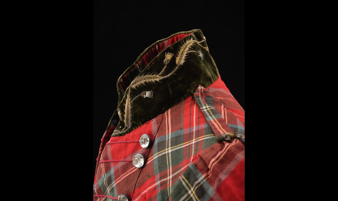 Detail of a red tartan jacket with an olive green velvet collar with embroidered thistle pattern