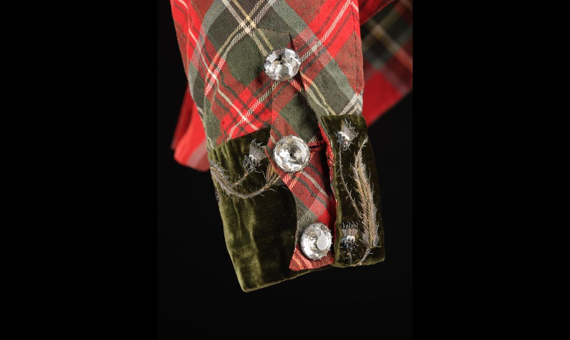 Detail of a red tartan jacket with an olive green velvet cuff and cut glass buttons.