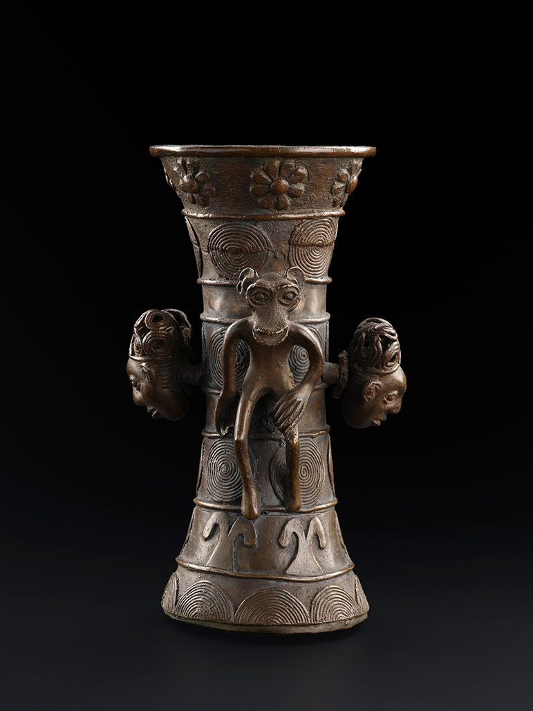 A brass vase or vessel with figures of monkeys or apes around it. There are also human faces emerging from the vessel.