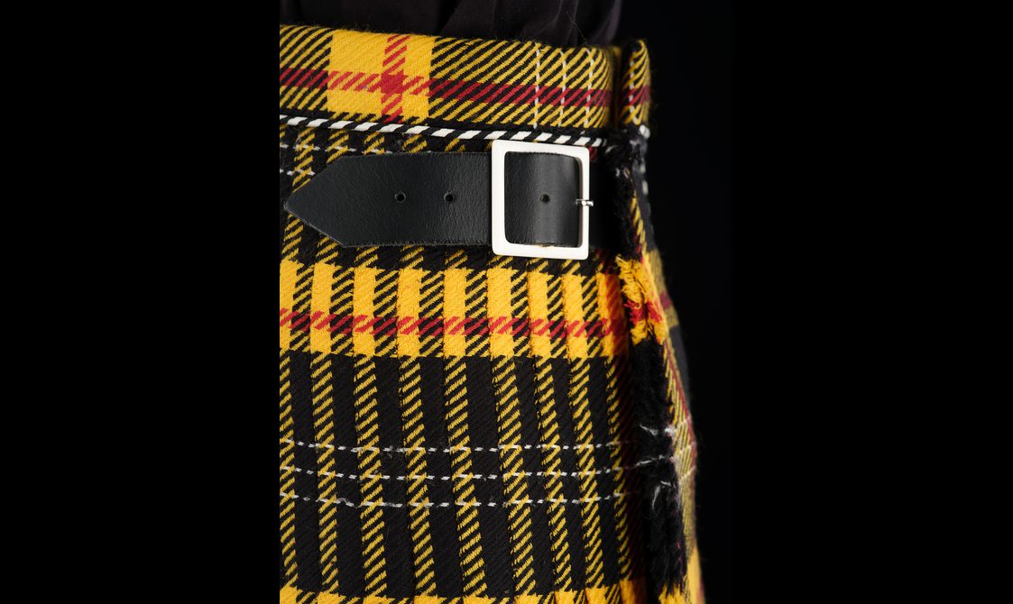 A detail of a yellow and black kilt with a leather buckle.
