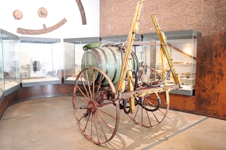 A horse drawn crop sprayer consisting of a barrel on a large wheeled instrument.