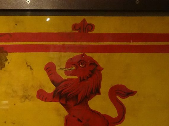A royal banner of Scotland showing a red lion framed in a double border with fleur-de-lis motifs.