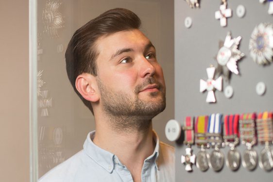 A visitor looking at a row of war medals in a glass museum case.