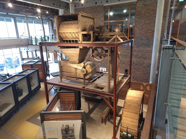 A large wooden mill machine on display in a museum gallery. It stretches the height of two floors.
