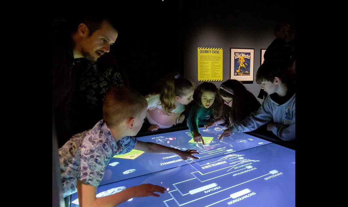 A group of children interacting with a large touchscreen in a museum exhibition