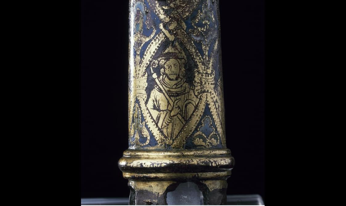 Closeup of detail on the grey-blue crozier staff, revealing a golden saint in a hood holding a crozier within a golden frame.