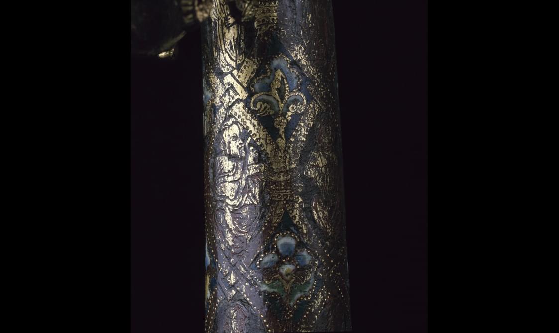 Closeup of the grey-blue crozier staff, revealing golden patterns of fleur-de-lis, flowers, and a saint.