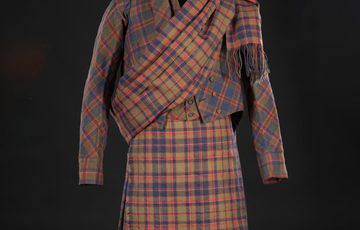 A man's tartan kilt suit in brown red tartan pattern with diagonally draped fabric over left shoulder