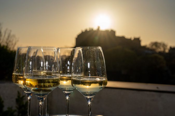 A close up of four glasses of white wine with a view of Edinburgh Castle in the background.