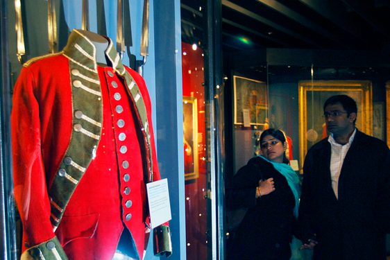 A picture of two visitors viewing a uniform displayed behind a glass case.
