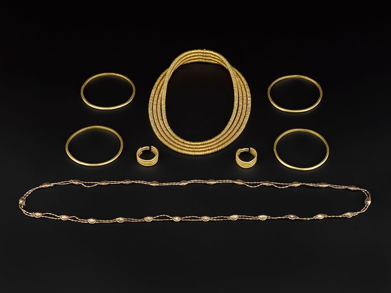 A collection of gold jewellery including four bangles, two necklaces, and a set of earrings set against a black background