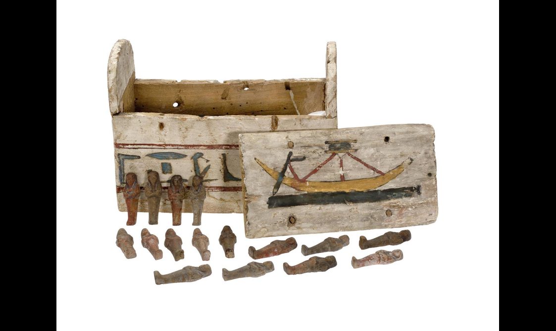 An old Egyptian wooden box with illustrations including a boat. Various small carved figures are arranged outside the box.