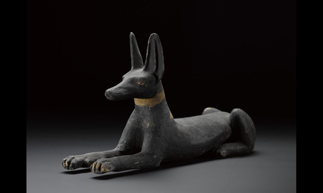 A wooden sculpture of a black jackal laying down with it's head held up.